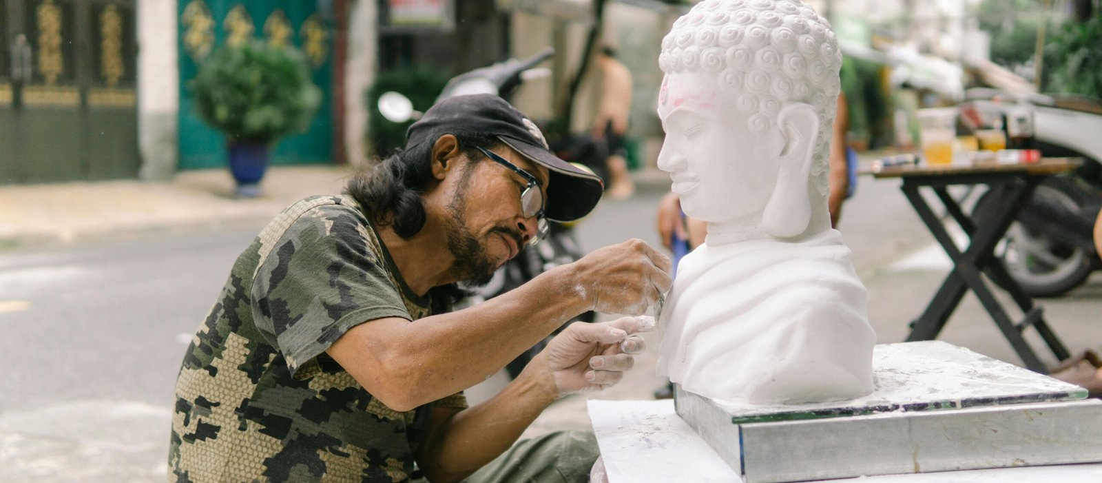 Artist sculpting a Buddha bust on a bustling street in Ho Chi Minh City, Vietnam.