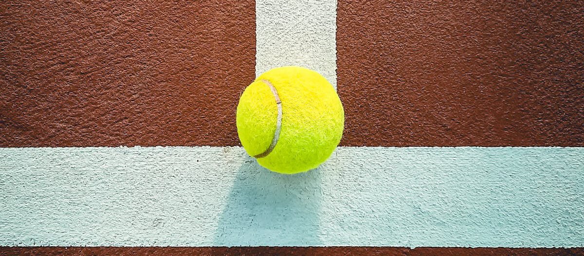 Tennis ball on a clay court highlighting its vibrant color and shadows. Ideal for sports concepts.