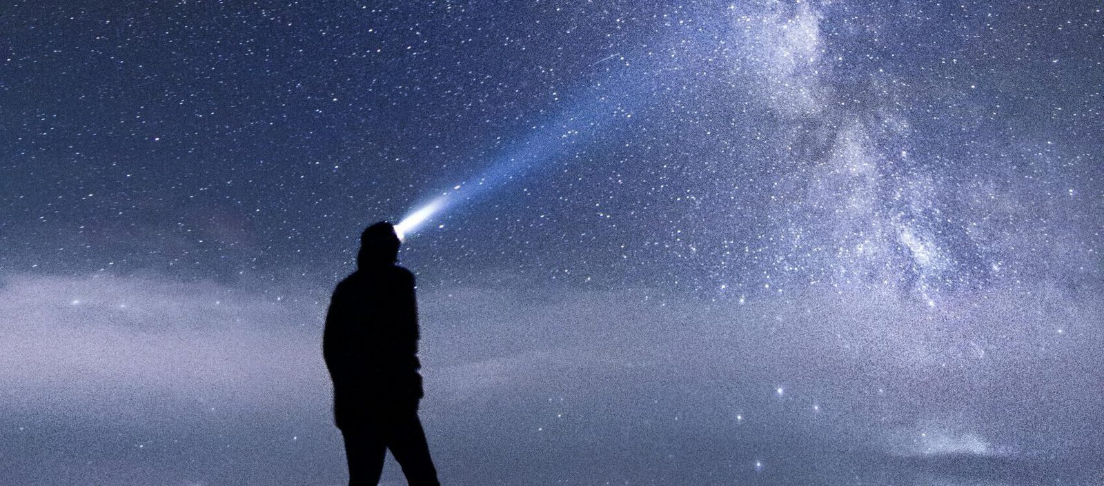 Silhouette of a person exploring the star-studded Milky Way sky at night in the mountains.