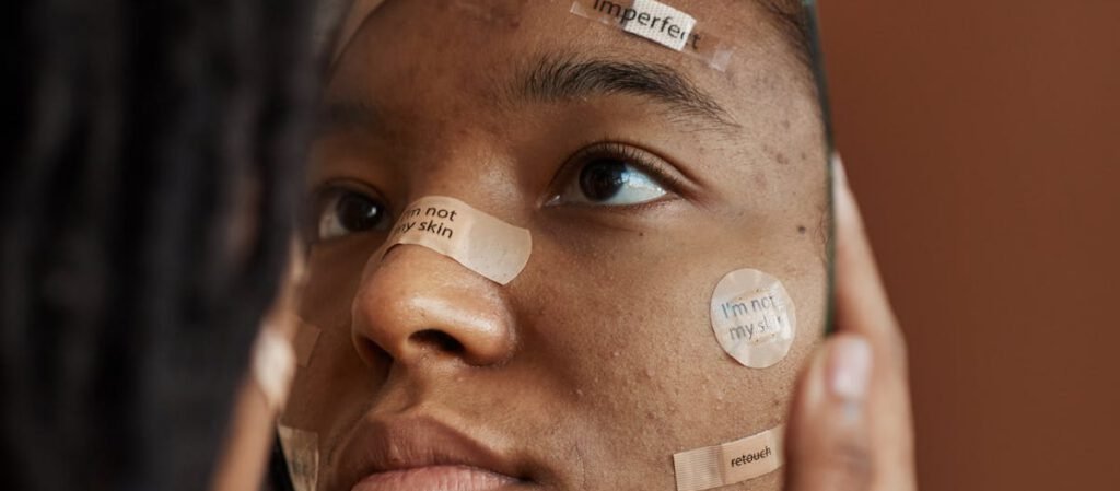 A young woman observes her reflection in a broken mirror with positive affirmations on band-aids.