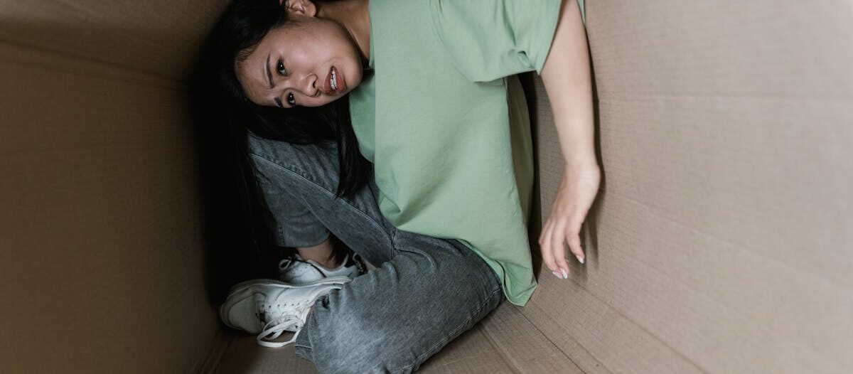 A woman trapped inside a cardboard box, symbolizing anxiety and fear.