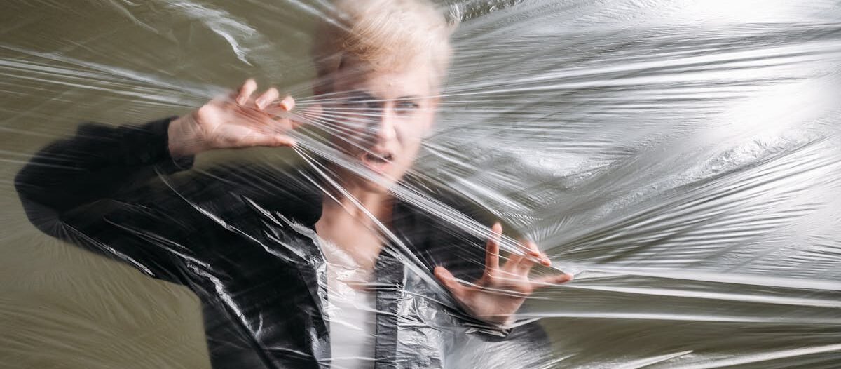 A woman pressed against a plastic sheet creating a sense of entrapment and surrealism.