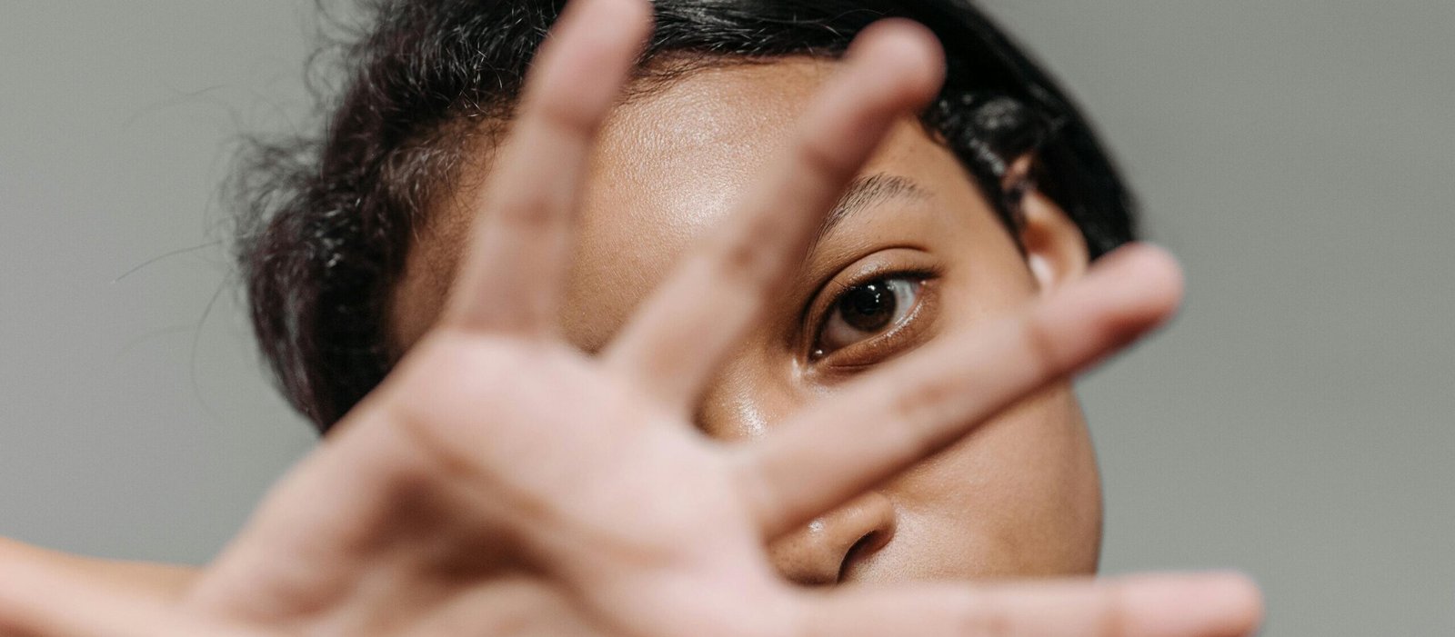 Intimate portrait of a woman partially covering her face with her hand against a gray background.
